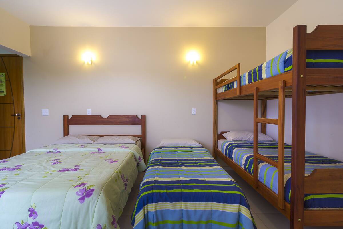 A room with two single beds and a bunk bed, equipped with wall-mounted lights.