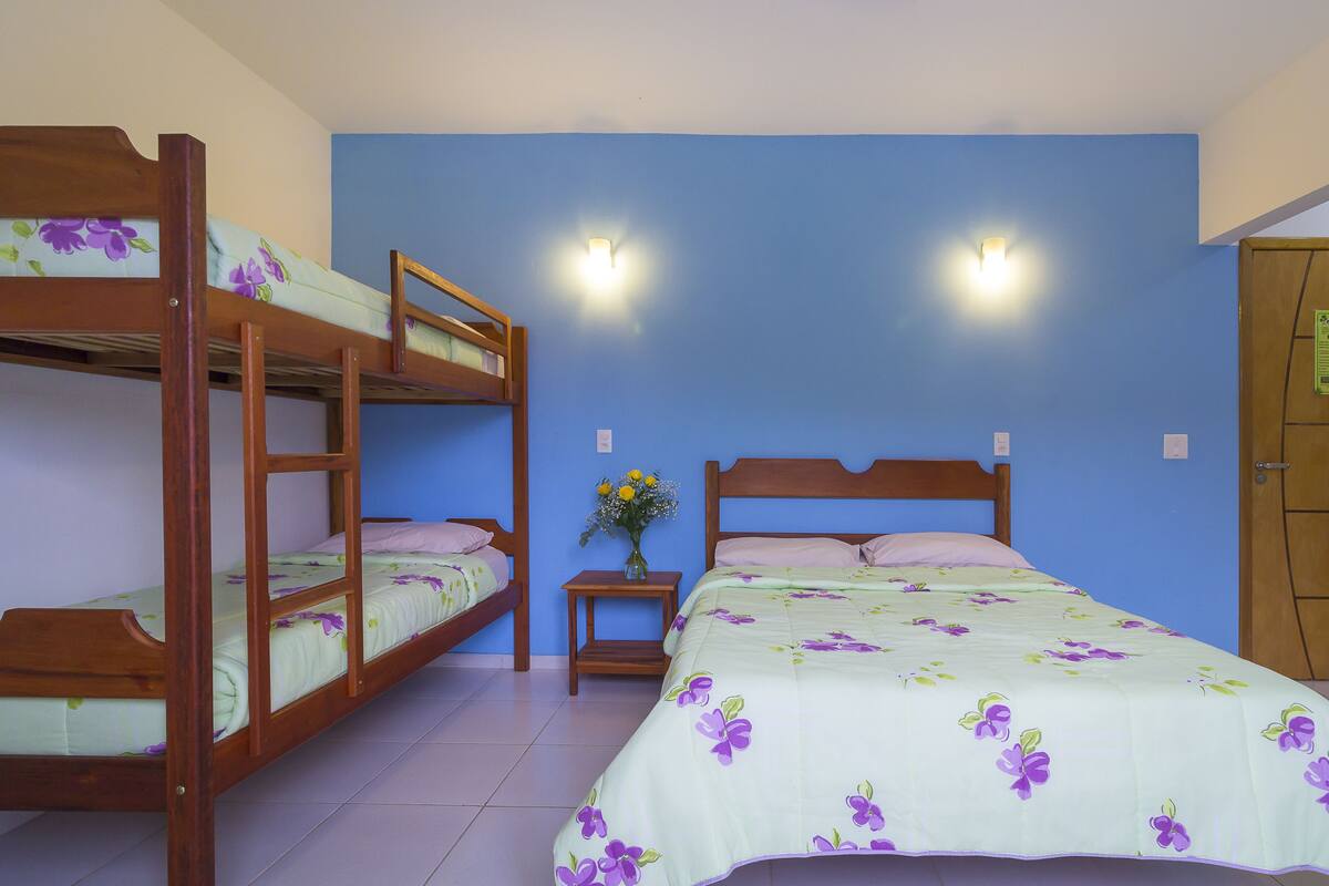 A room with bunk beds, a single bed, a nightstand with a vase of flowers, and two wall-mounted lights.