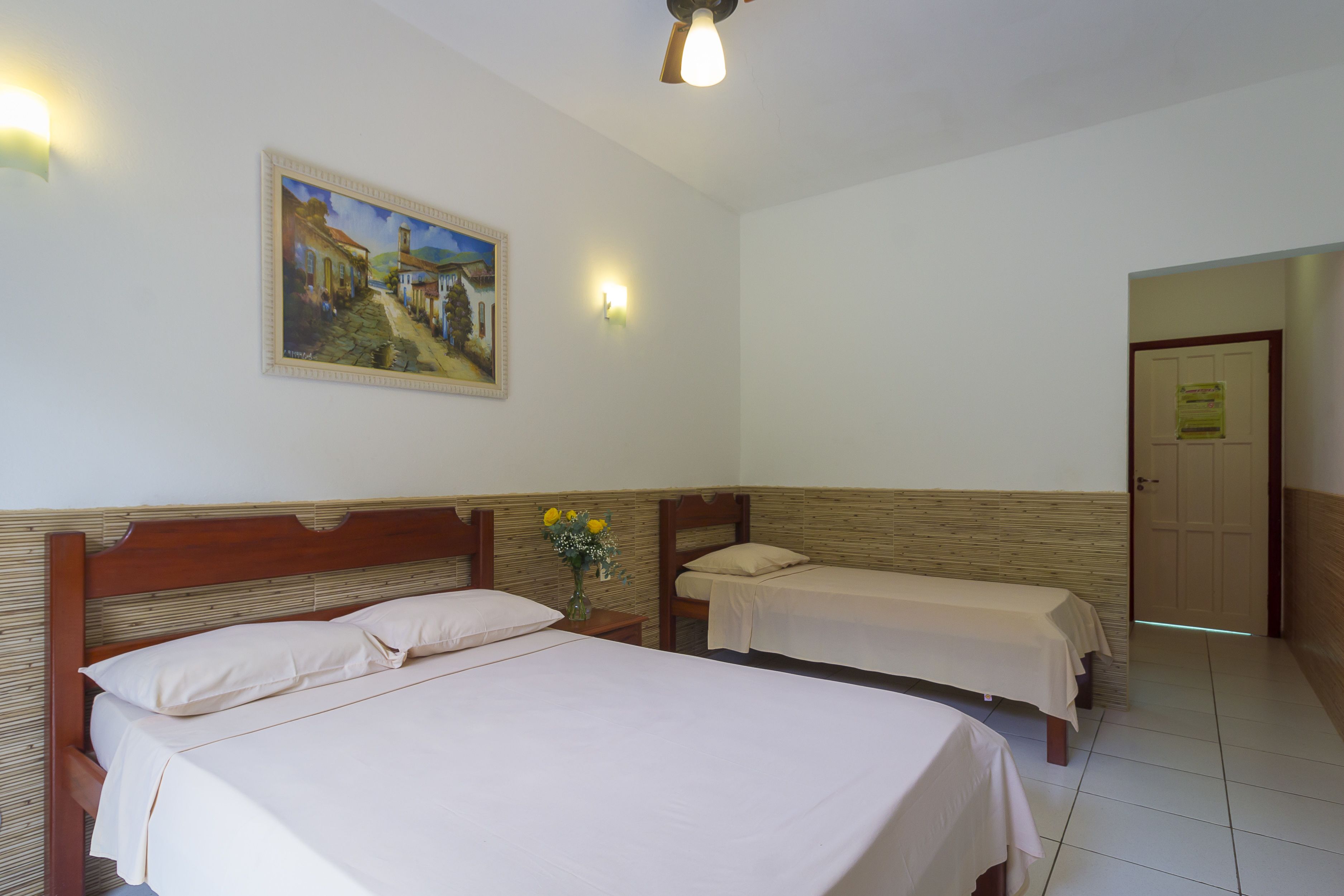 Een hotelkamer met twee bedden, een schilderij aan de muur en een deur naar een andere kamer.