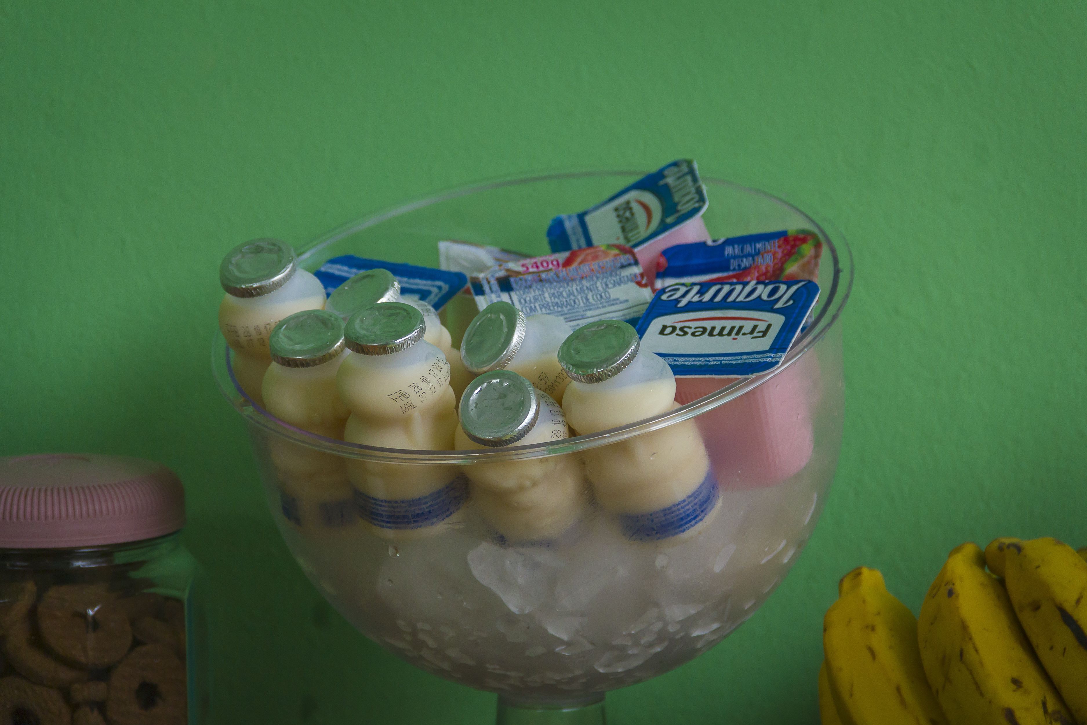 A glass bowl filled with ice and bottles, with a jar of cookies and bananas in the background.