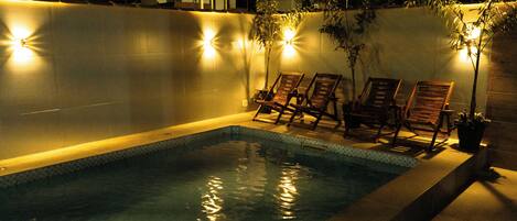 A swimming pool with two lounge chairs and wall-mounted lights.