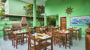Un restaurant avec des tables et des chaises en bois, un four en briques et un mur végétal orné d’une affiche.