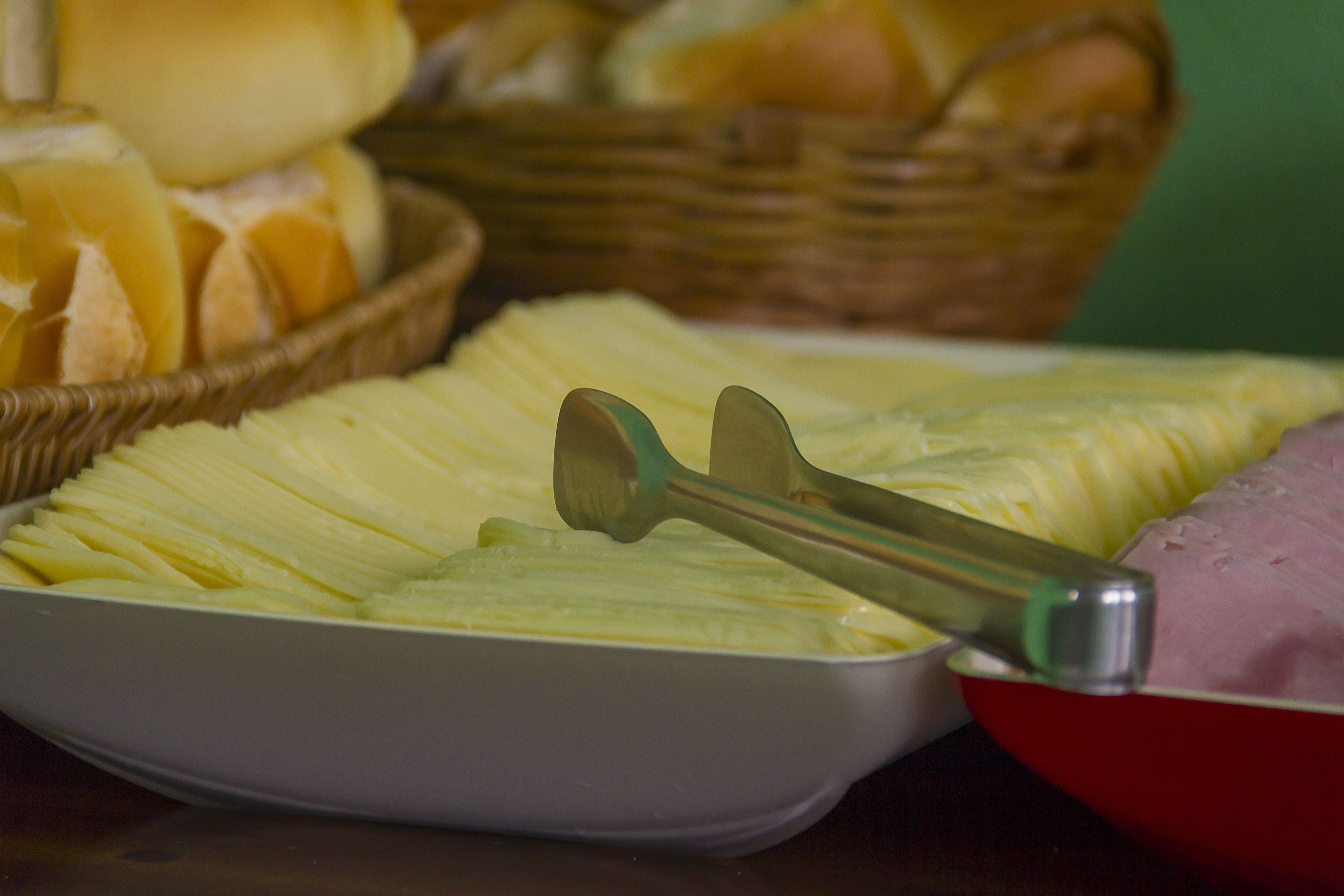 A tray of sliced vegetables and a bowl of meat, with a basket of bread in the background.