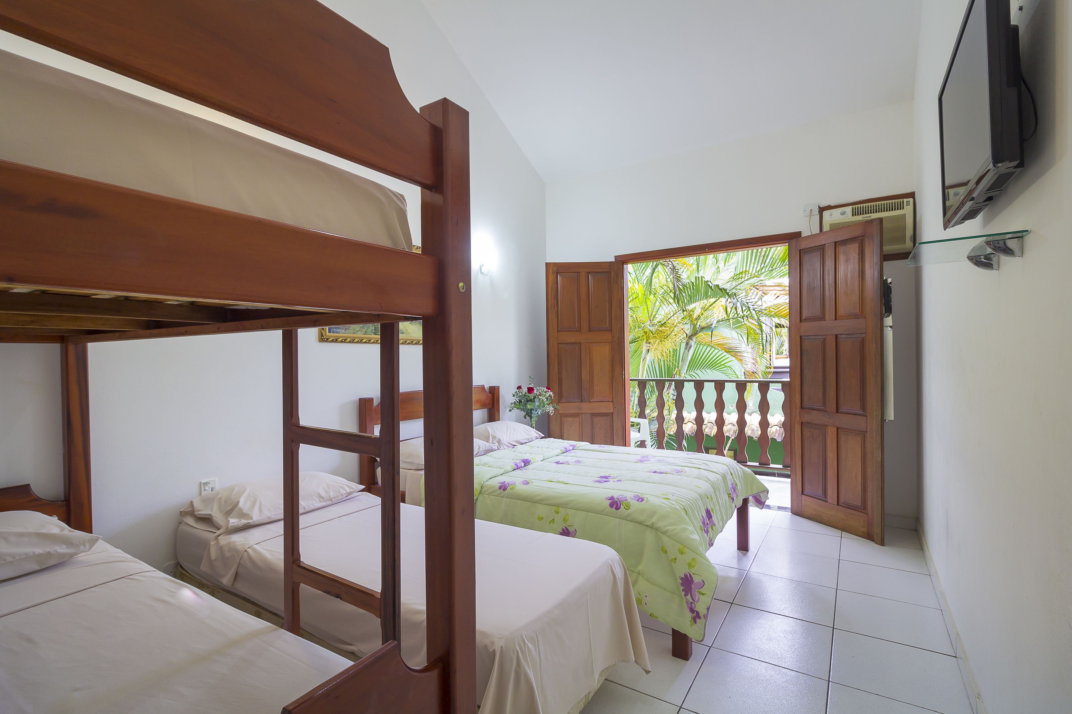 A bedroom with two single beds, a bunk bed, a TV, and a balcony with a wooden door.