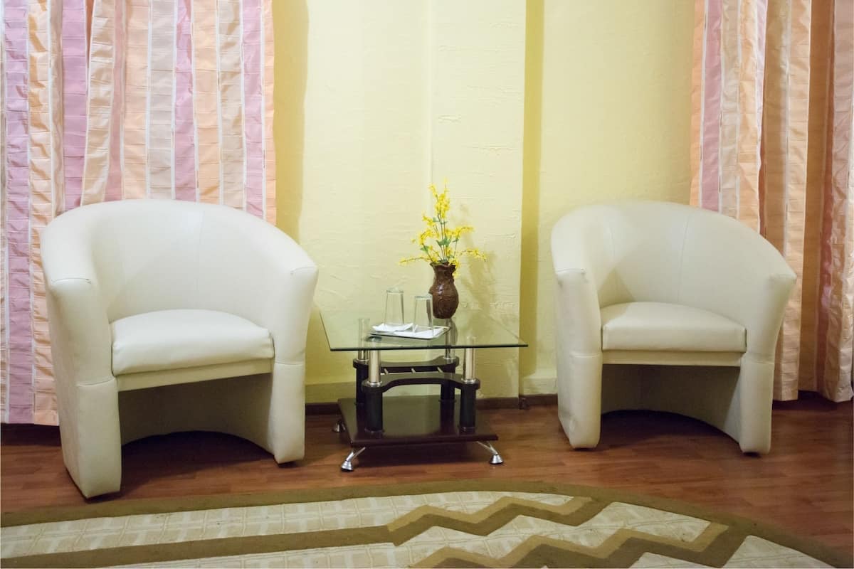 Um quarto com duas poltronas brancas, uma mesa de vidro pequena com um vaso de flores amarelas e um tapete estampado no chão.