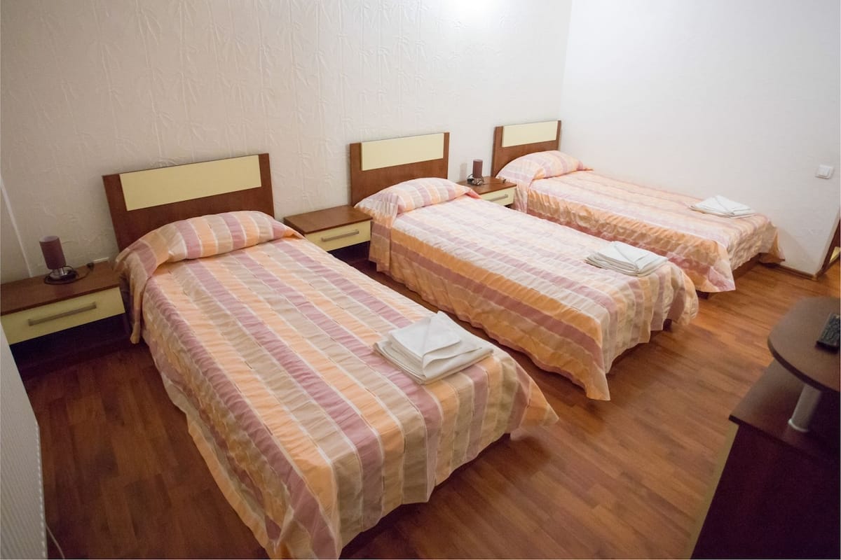 Quarto de hotel com três camas de solteiro, piso de madeira e uma pequena mesa redonda.