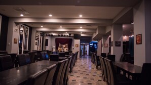 Un restaurante con una barra larga y varias mesas, suelo de baldosas y un escenario con cortinas al fondo.