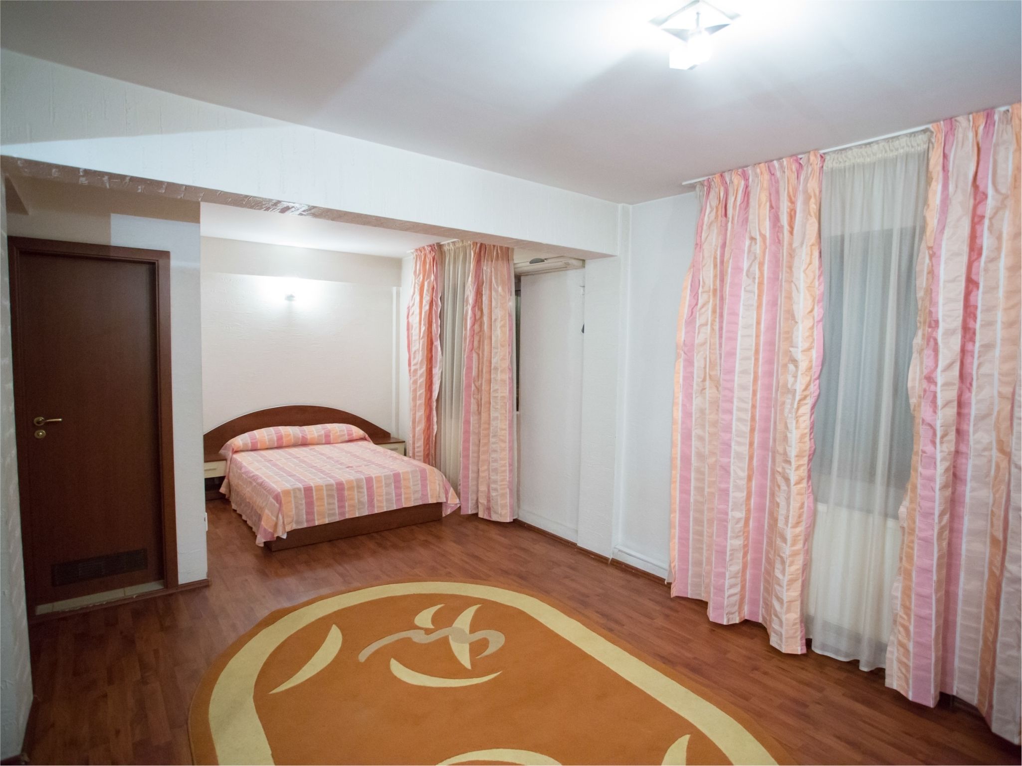 A bedroom with a wooden floor, a bed with striped bedding, a door, and curtains.