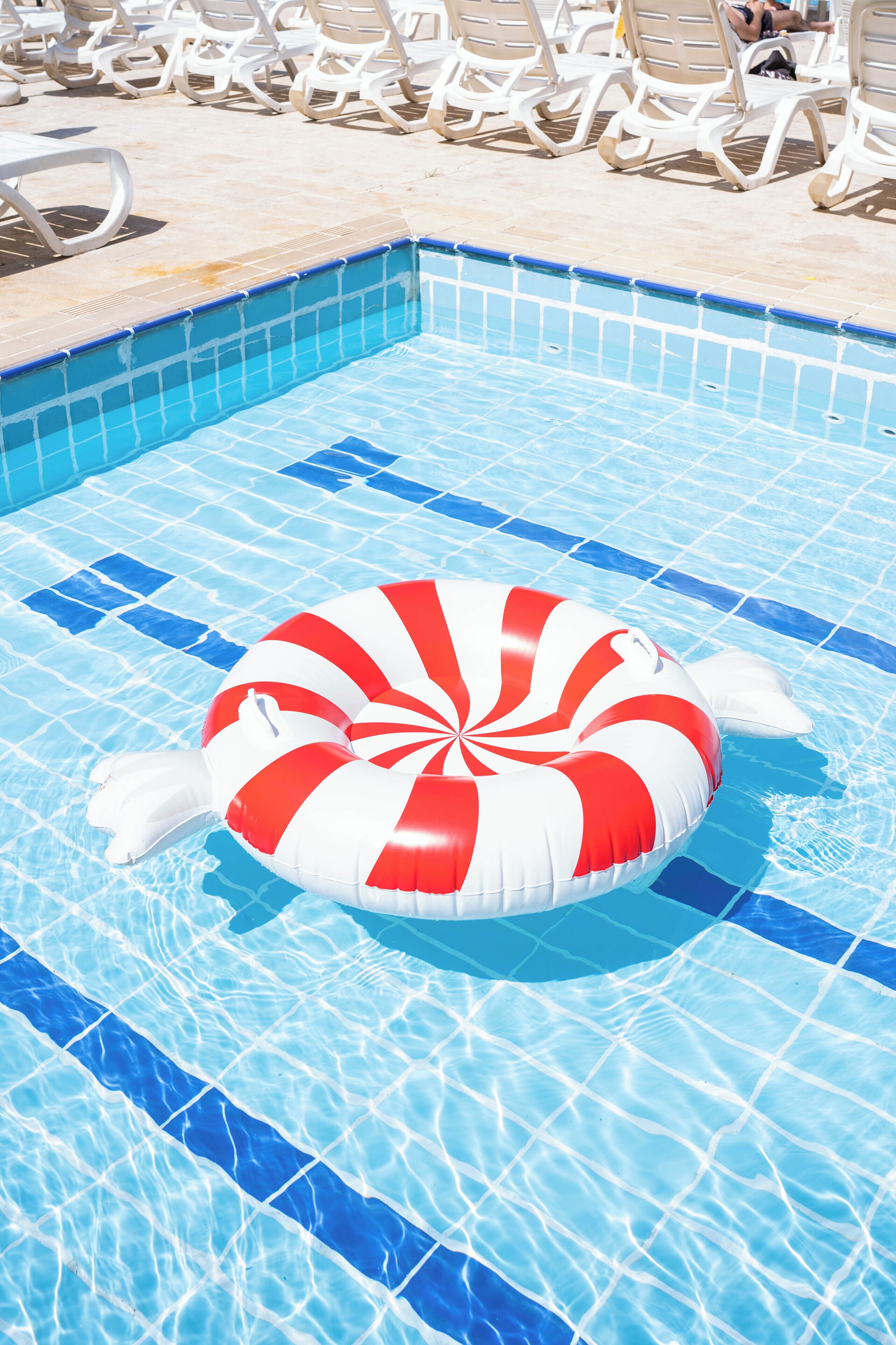 A swimming pool with a red and white striped floatation device in the water.