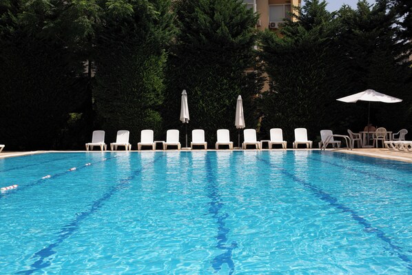 A swimming pool with white lounge chairs and umbrellas, surrounded by trees.