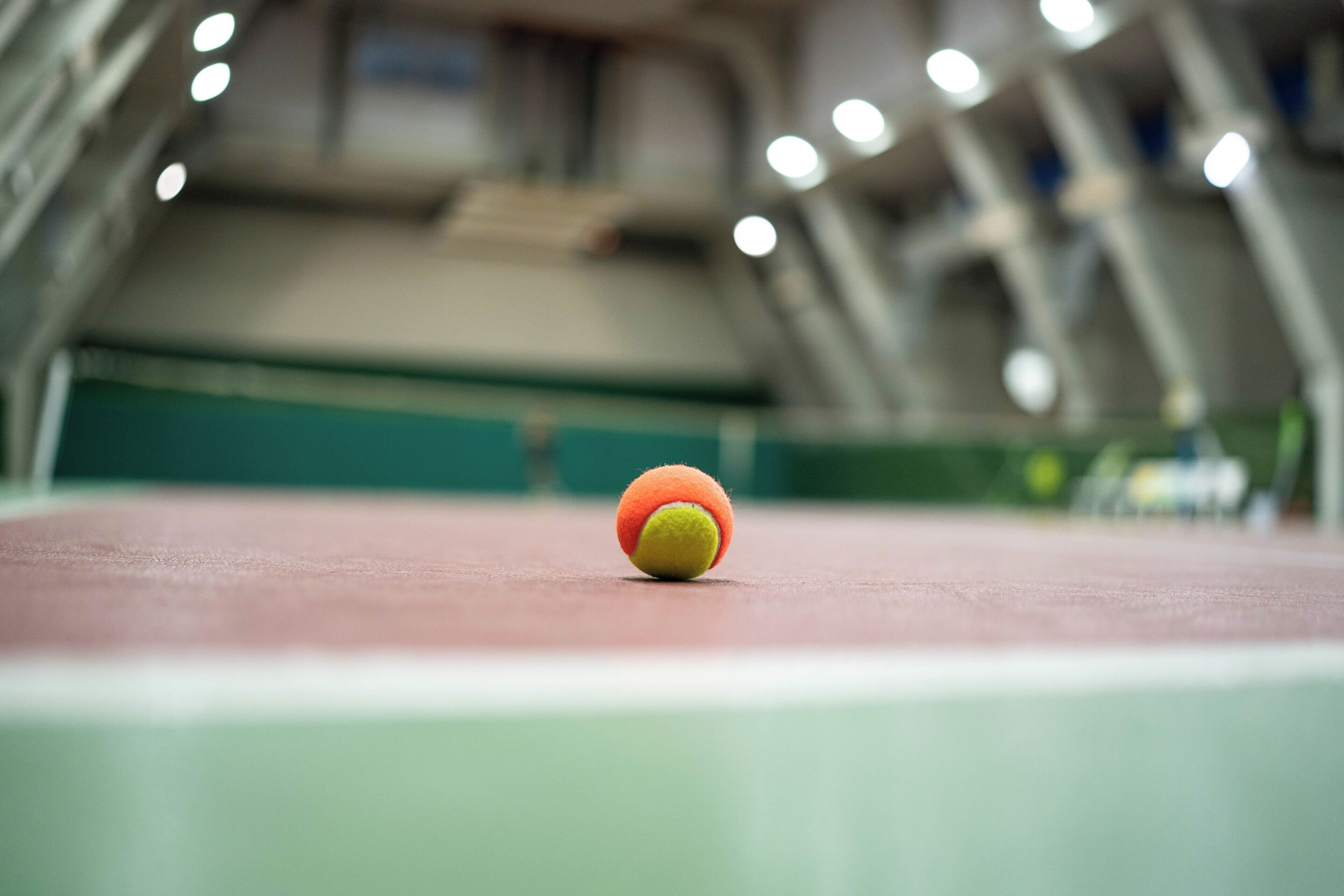 En tennisbold på en tennisbane med et grønt net og en uskarpt baggrund af et stadion.