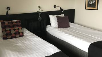 Una habitación de hotel con dos camas, una mesita de noche con lámpara, un jarrón con flores y un cuadro en la pared.