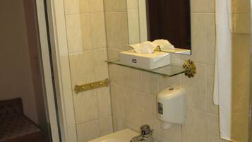 Un bany amb un lavabo blanc, una petita estant de vidre, una caixa de mocadors i un vàter.