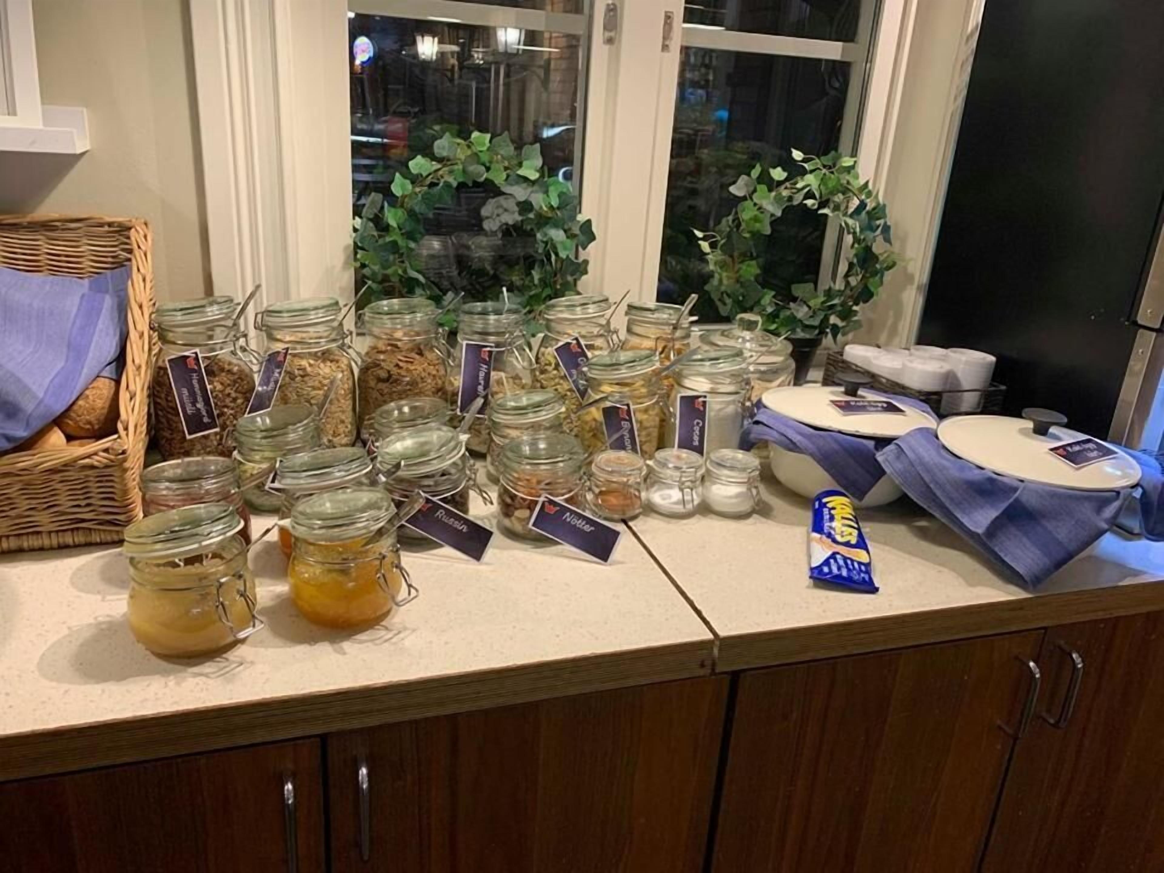 Una encimera de cocina con varios frascos de alimentos, un cesto de pan y una pequeña bolsa de aperitivos.