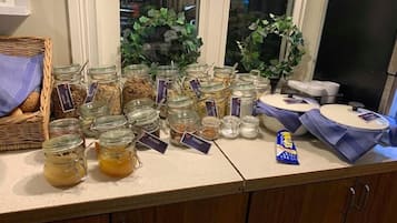 En köksbänk med olika burkar innehållande matvaror, en korg med bröd och ett litet paket med snacks.