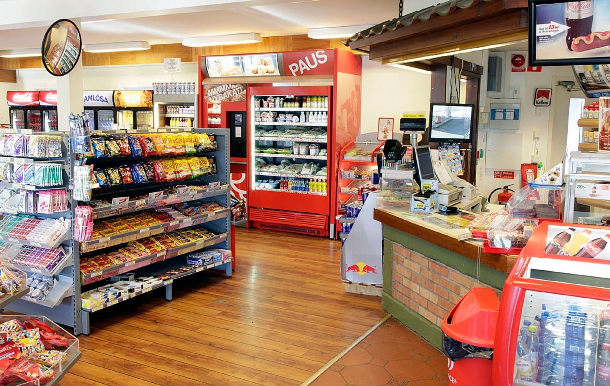 Interior de um supermercado com corredores repletos de lanches, bebidas e produtos de limpeza.