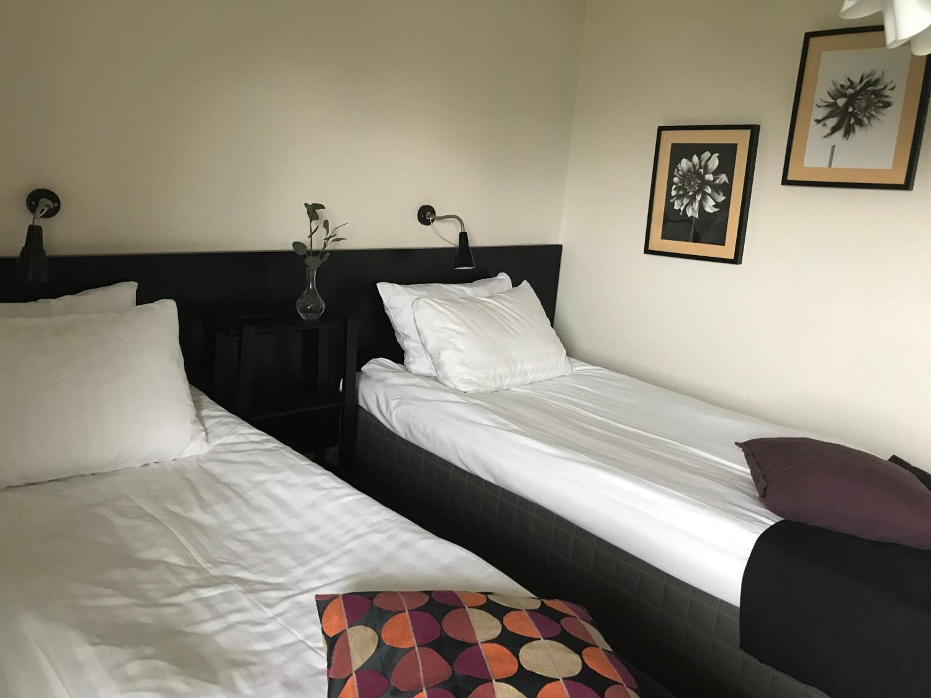 A hotel room with two single beds, a nightstand with a vase, and a wall-mounted lamp.