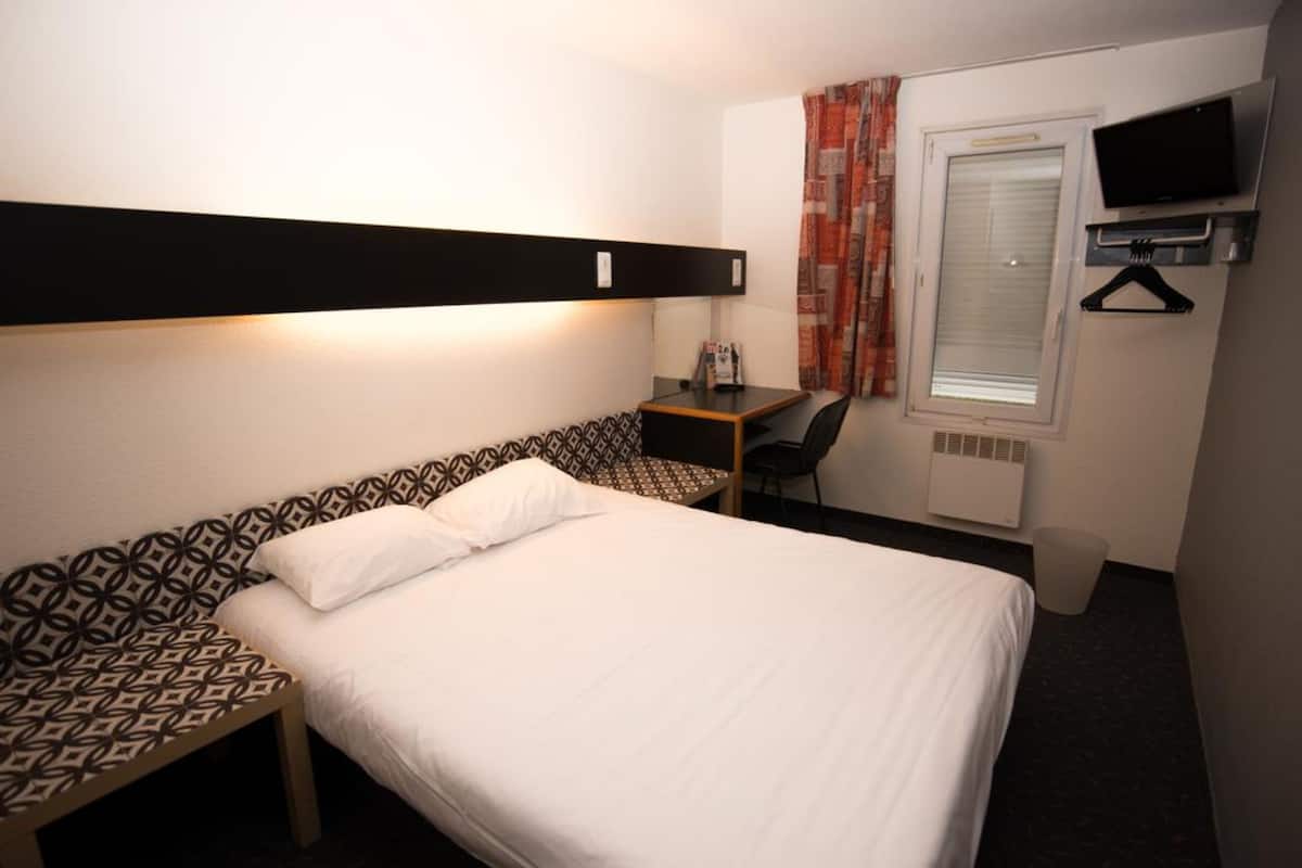 Une chambre d’hôtel équipée d’un lit, d’un bureau, d’une chaise, d’une télévision et d’une fenêtre avec des rideaux.