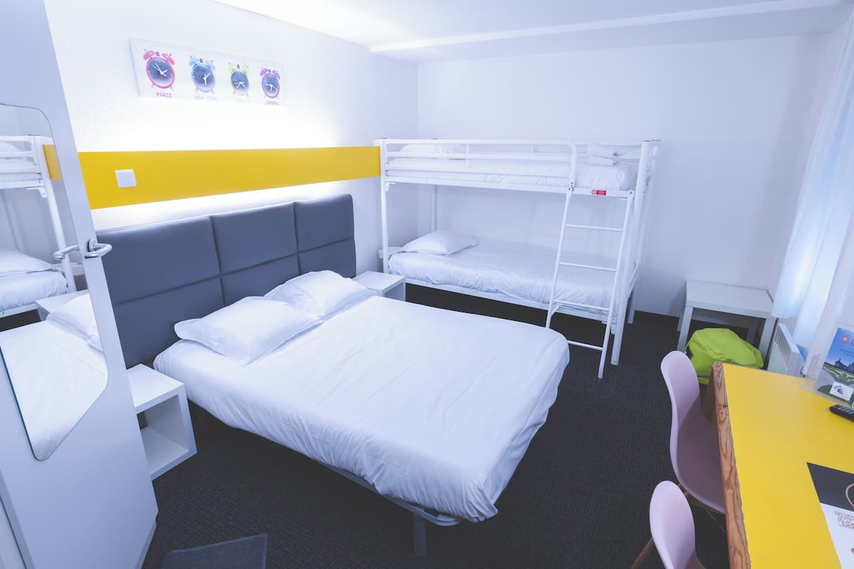 Une chambre d’hôtel avec des lits superposés, un bureau, une chaise et un lit avec une tête de lit.