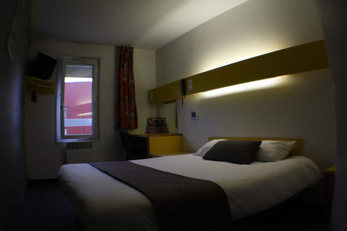 Une chambre d’hôtel équipée d’un lit, d’un bureau, d’une chaise, d’une télévision et d’une fenêtre avec des rideaux.
