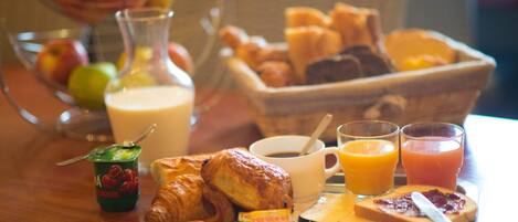 Bandeja de desayuno con cruasanes, pasteles, un vaso de jugo de naranja, una taza de café y un bol de fruta.