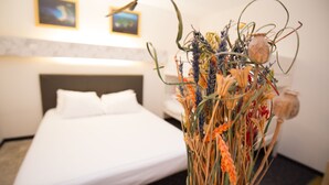 Una habitación de hotel con una cama, un jarrón con flores secas y una pared con dos cuadros enmarcados.
