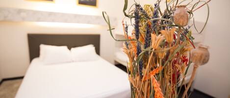 Una habitación de hotel con una cama, un jarrón con flores secas y una pared con dos cuadros enmarcados.