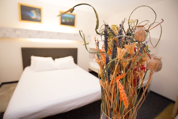 Una habitación de hotel con una cama, un jarrón con flores secas y una pared con dos cuadros enmarcados.