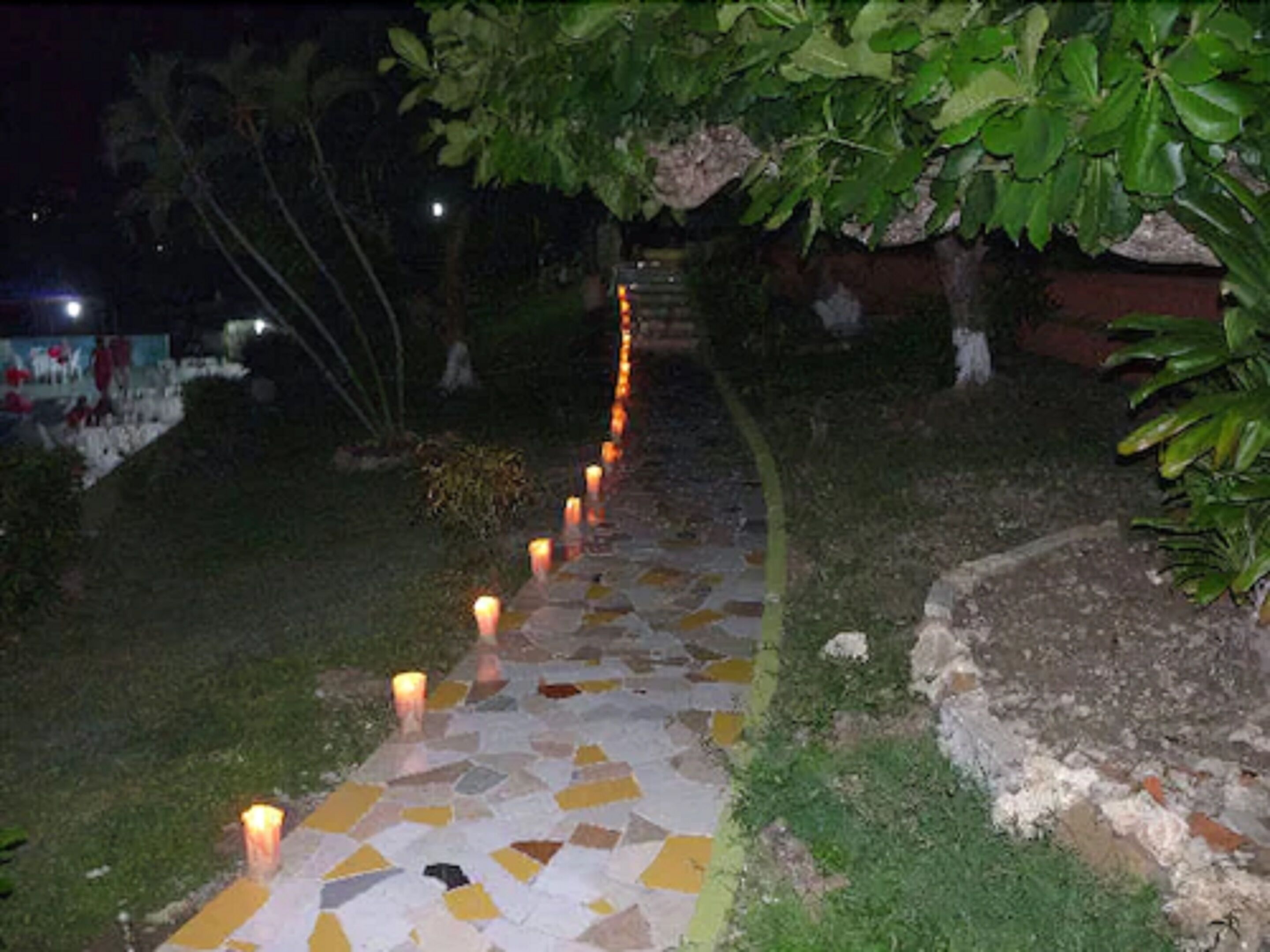 Un sendero con un diseño de mosaico, bordeado de velas y rodeado de follaje.