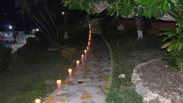Un sendero con un diseño de mosaico, bordeado de velas y rodeado de follaje.