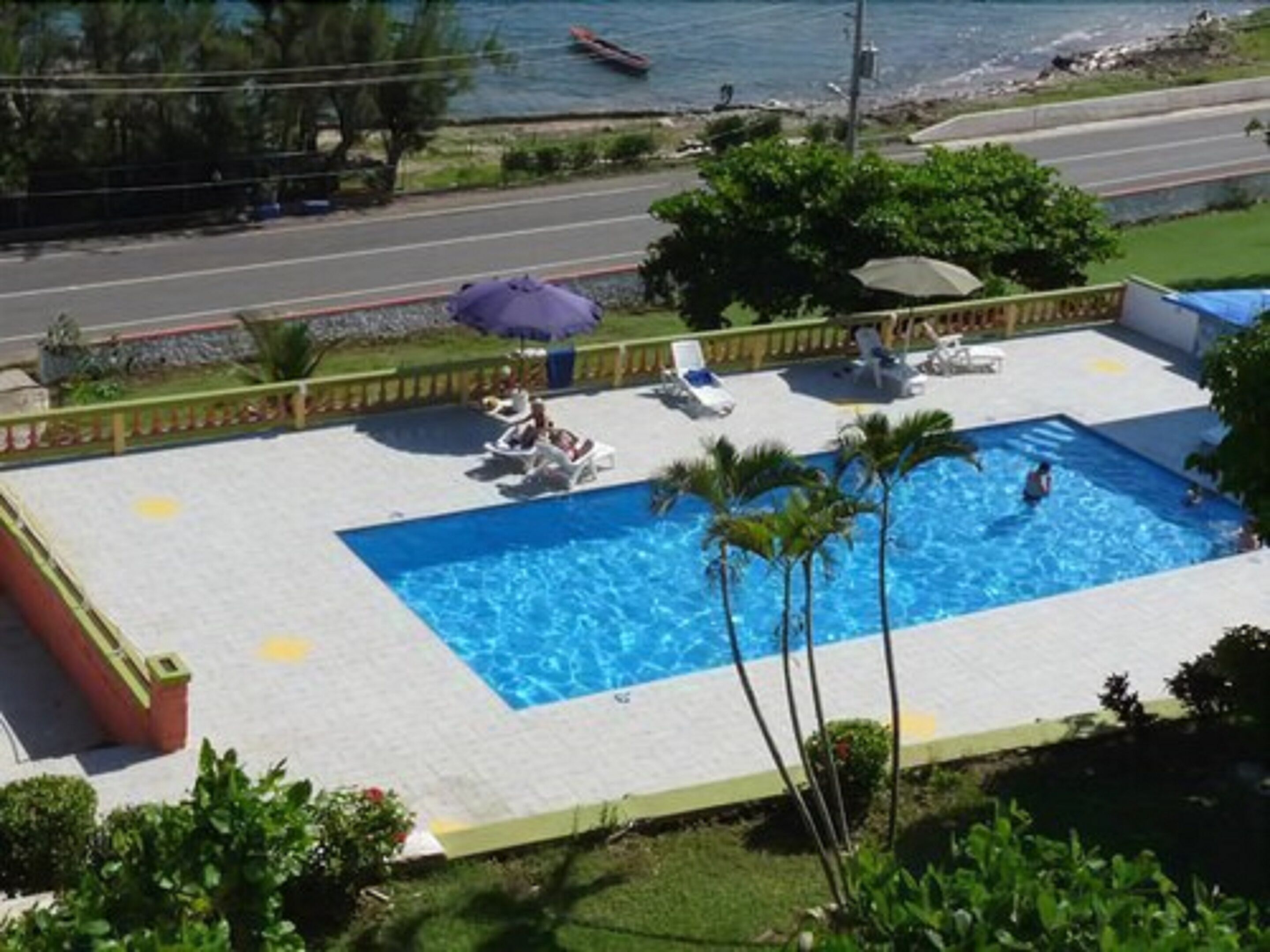 A swimming pool with lounge chairs and umbrellas, surrounded by greenery and a view of the sea.