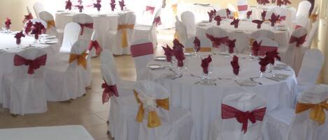 A banquet hall with round tables set for a formal event, each with white tablecloths and chairs adorned with red and yellow sashes.