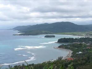 A coastal landscape with a beach, a small town, and hills in the background. - Casa Maria Hotel (Port Maria)
