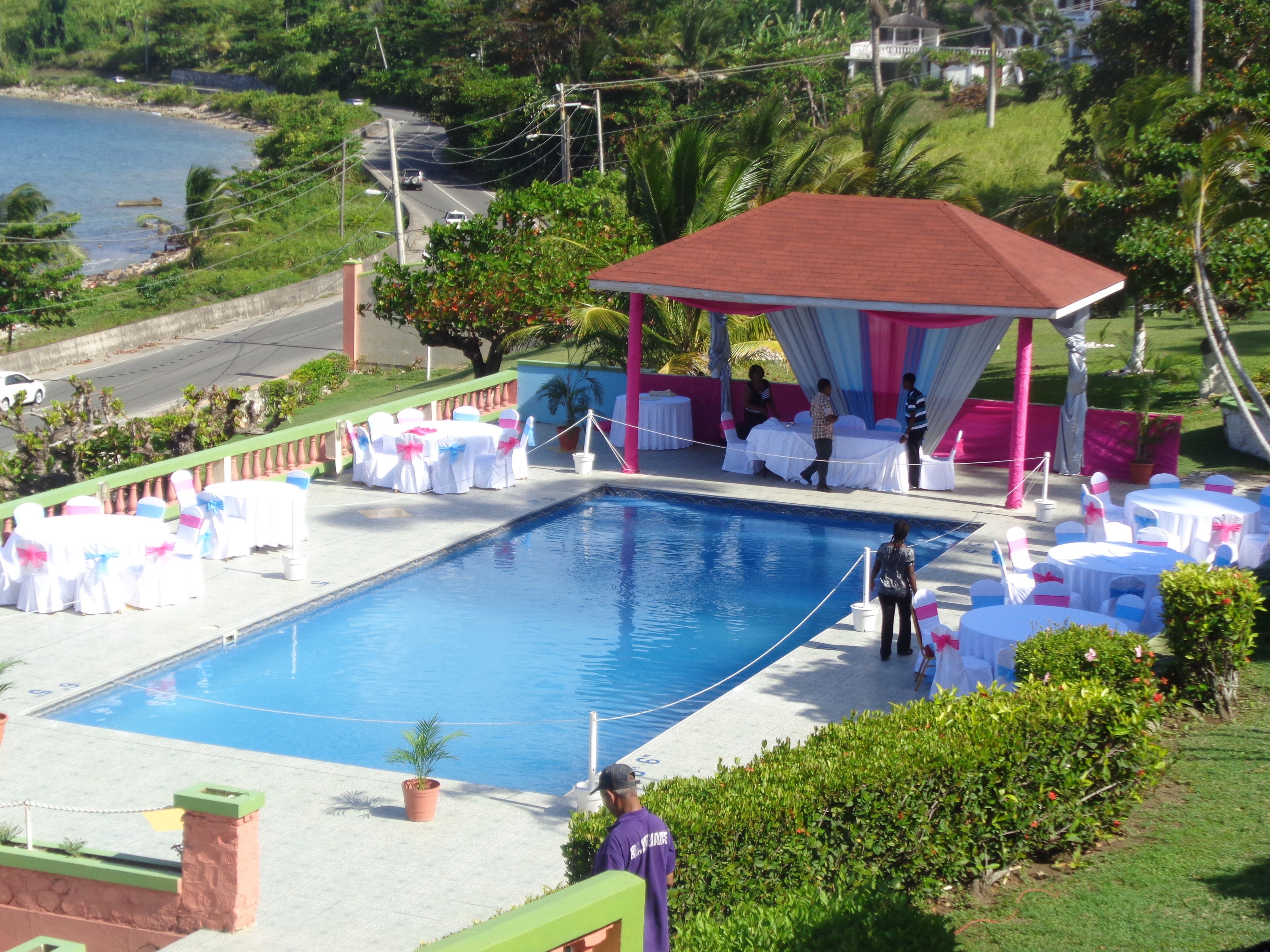 Zona de piscina con área de descanso cubierta, mesas y sillas.