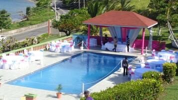 Zona de piscina con área de descanso cubierta, mesas y sillas.