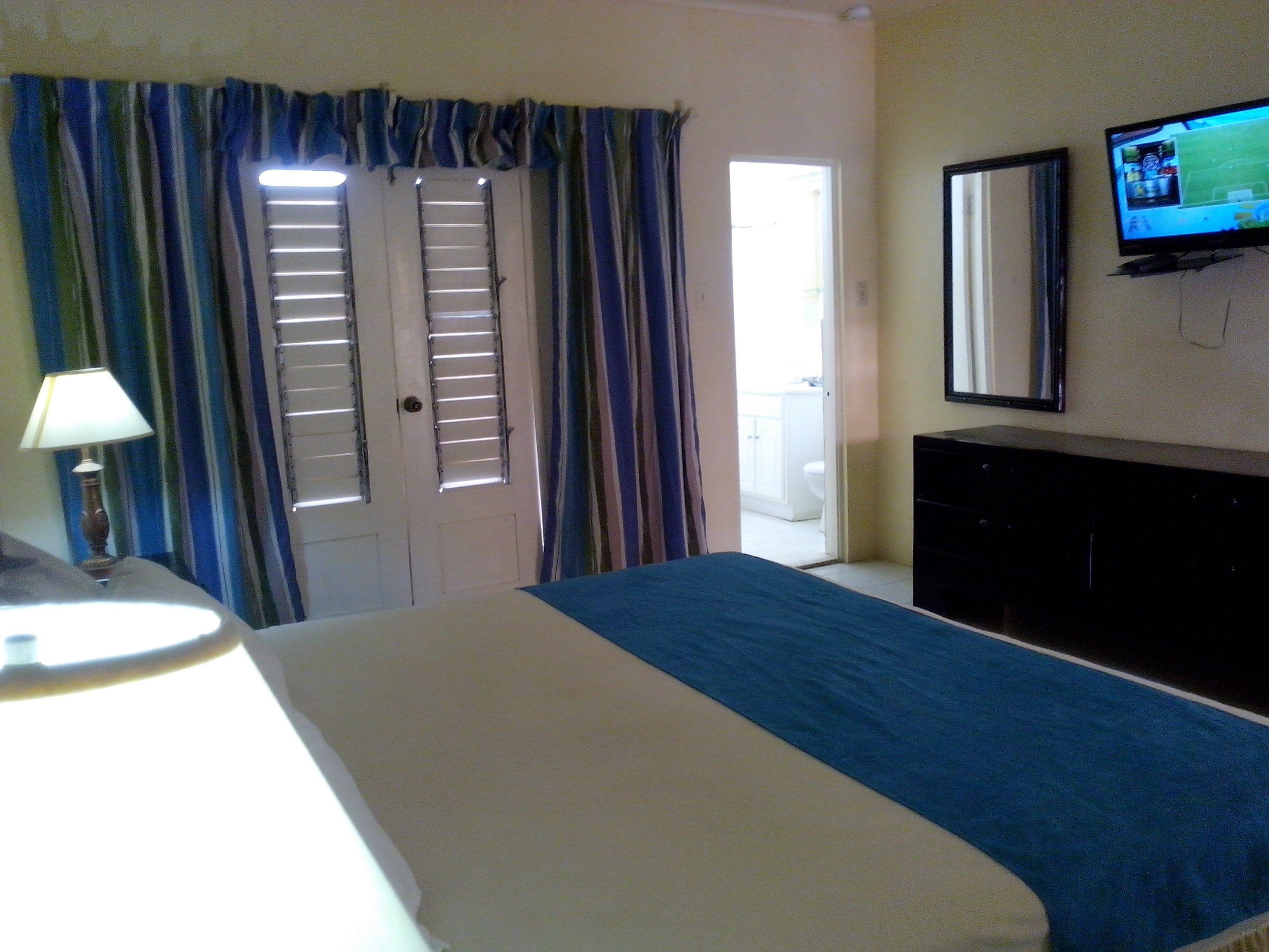 Un dormitorio con cama, televisor, cómoda y ventana con cortinas.