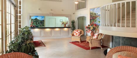 A spacious living area with high ceilings, a kitchen in the background, and a balcony with a railing.