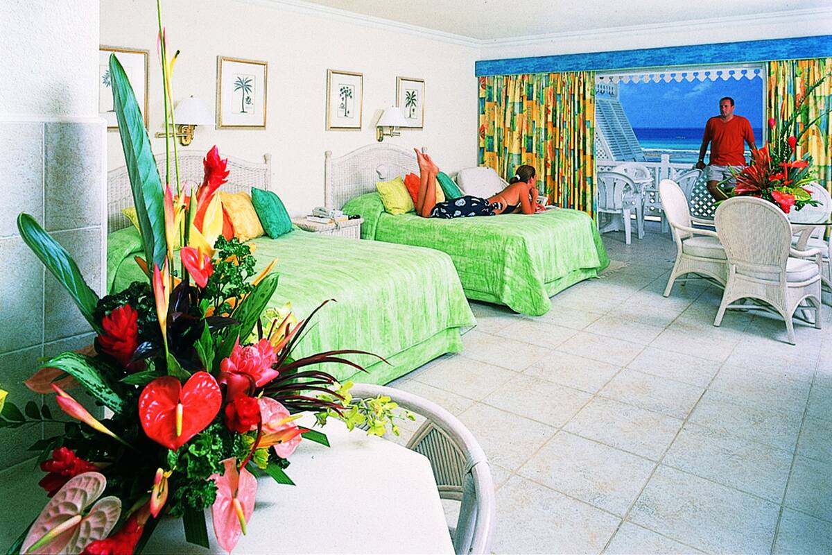 A hotel room with two beds, a dining area, and a view of the ocean.