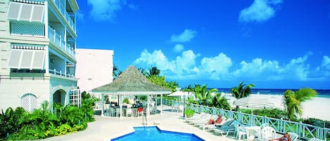 A pool area with lounge chairs and a gazebo, overlooking a beach.