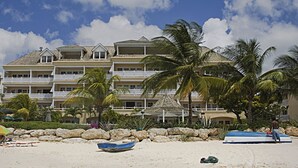 Un hotel frente a la playa con varios balcones, palmeras y una playa de arena.