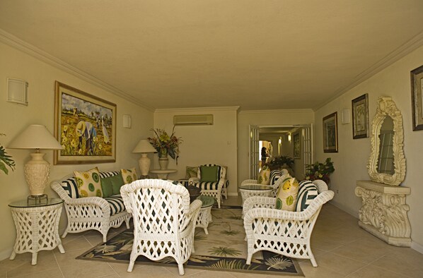 A spacious living room with wicker furniture, a large painting, and a mirror on the wall. - Coral Sands Beach Resort (Worthing)