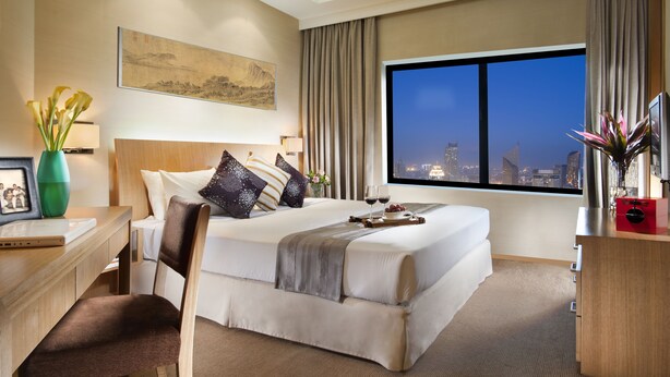 A hotel room with a large bed, a desk with a laptop, a chair, a TV, and a view of the city at night. - Somerset International Building Tianjin (Tianjin)