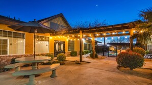 A patio area with a table and benches, a covered seating area, and a building with a dark door and string lights. - Comfort Inn & Suites Mojave (Mojave)