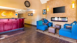 A lobby with a reception desk, blue seating area, a flat-screen TV mounted on the wall, and a clock on the wall. - Comfort Inn & Suites Mojave (Mojave)