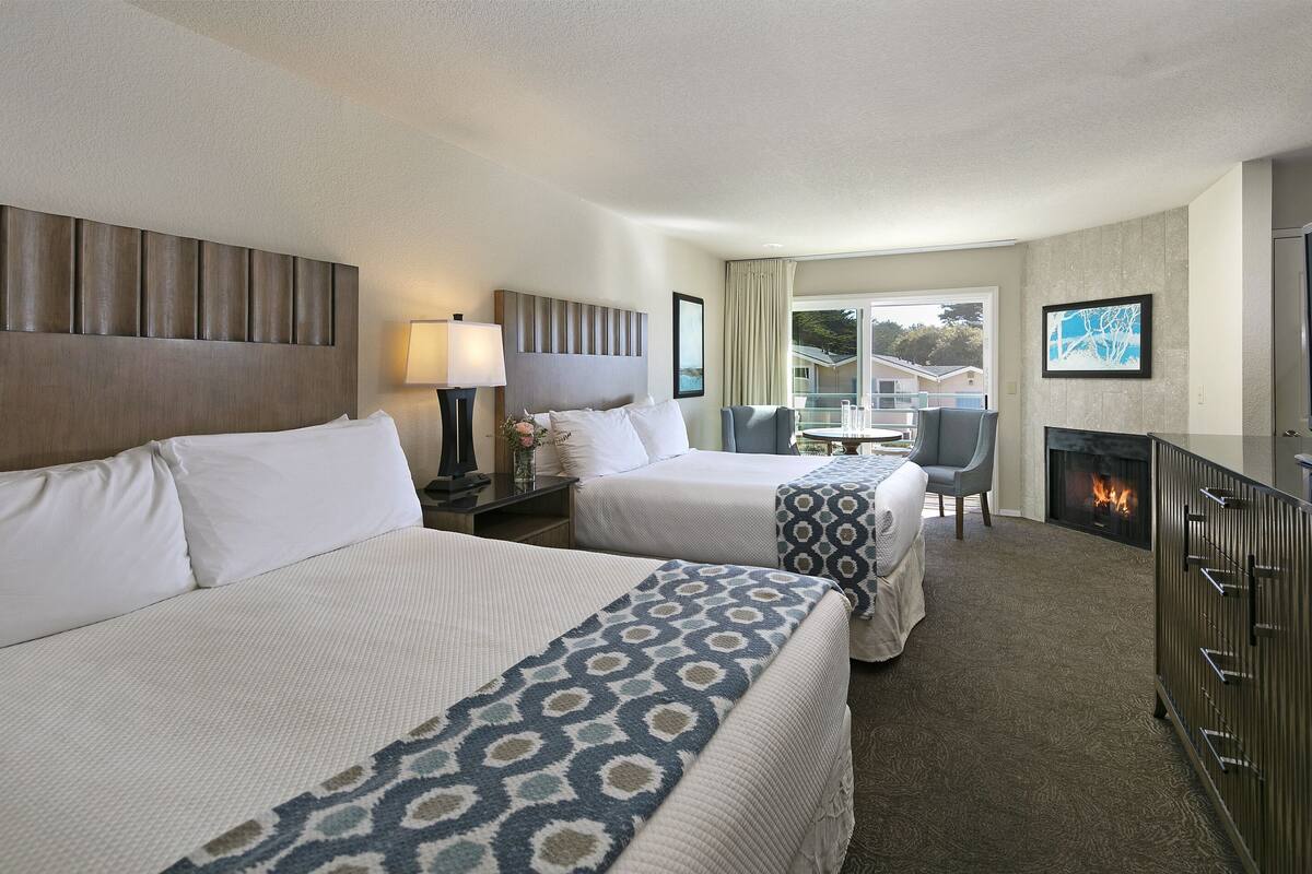 A hotel room with two beds, a TV, a fireplace, and a view of the outside.
