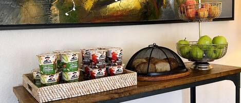 Uma mesa de madeira com aveia Quaker, uma cesta de frutas, uma cesta de arame e uma tigela de maçãs.