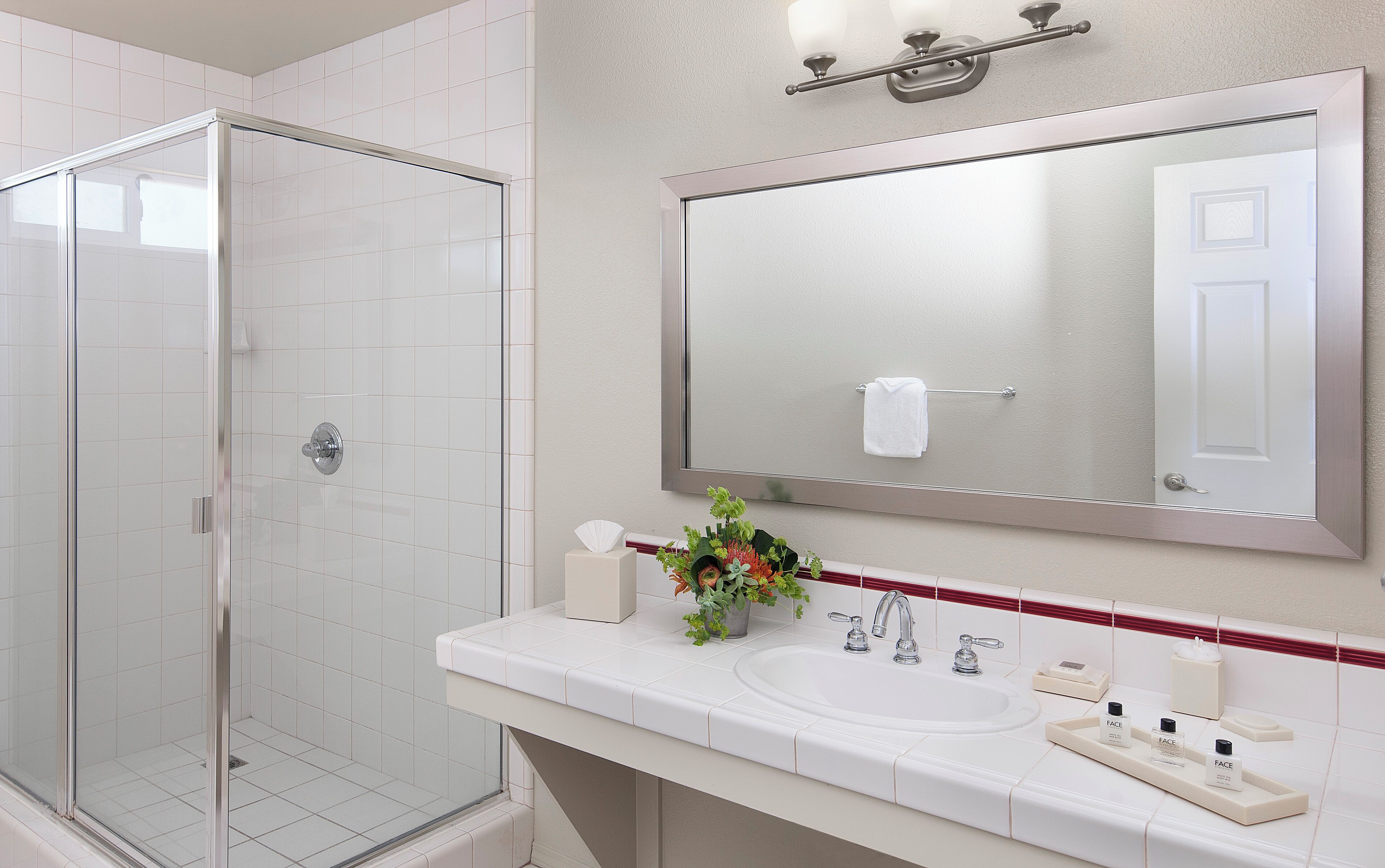 A modern bathroom with a glass shower enclosure, a large mirror, and a white sink with toiletries.