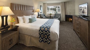 Habitación de hotel con una cama grande, dos sillones, un televisor, chimenea y vistas al exterior.