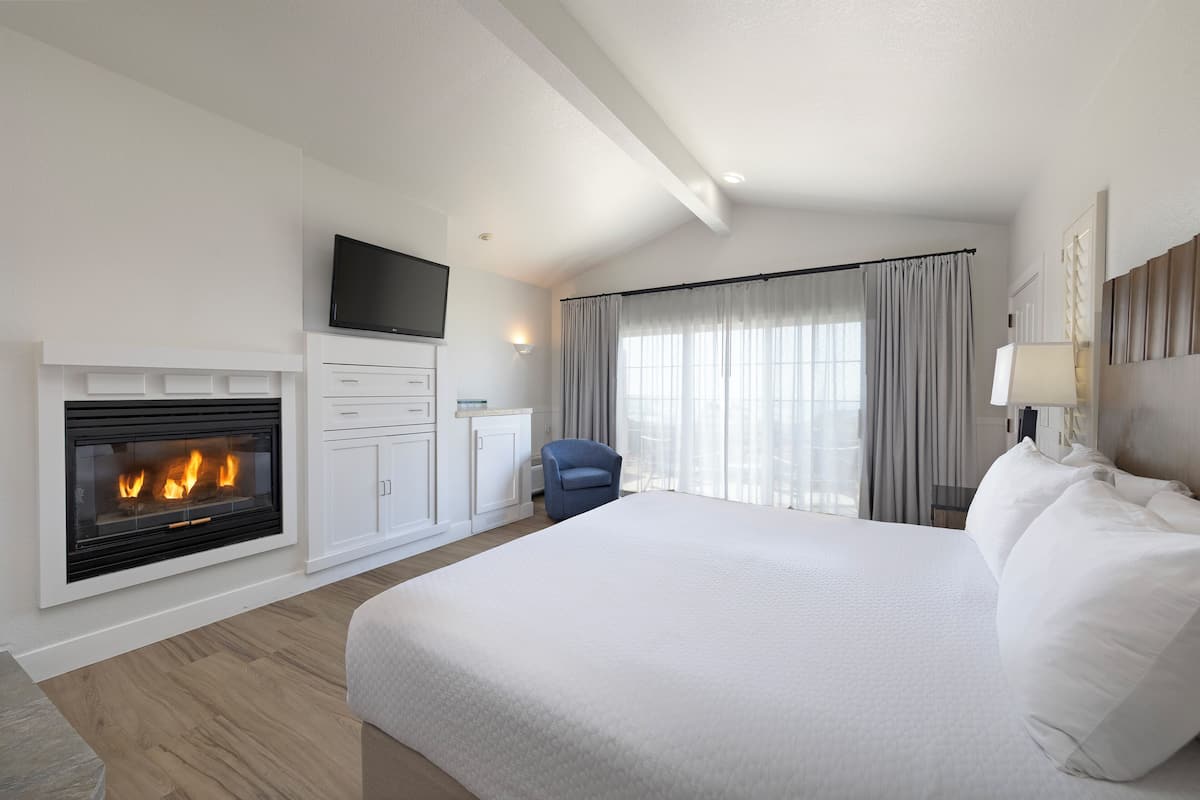 A hotel room with a large bed, a fireplace, a flat-screen TV, a desk, and a chair.