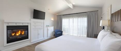 Ein Hotelzimmer mit einem großen Bett, einem Kamin, einem Flachbildfernseher, einem Schreibtisch und einem Sessel.